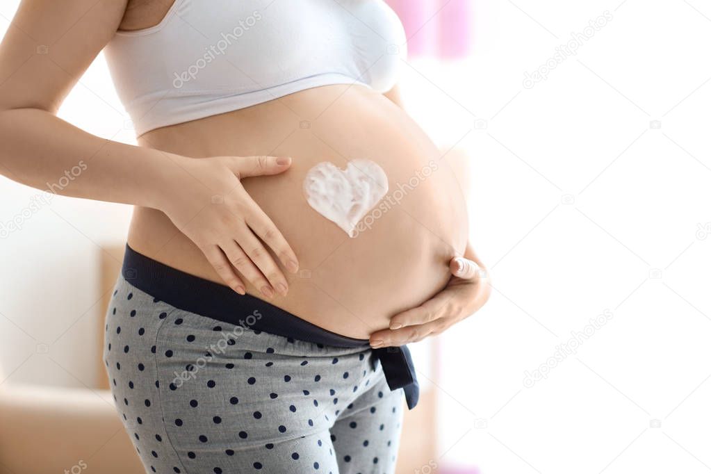 Heart painted with cream on pregnant woman's belly against blurred background, closeup