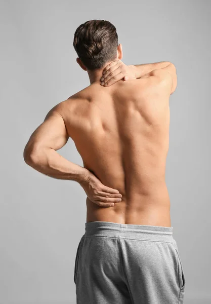 Mladý muž trpí bolesti krku na světlé pozadí — Stock fotografie