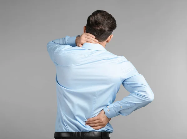 Jonge man die lijden aan nekpijn op grijze achtergrond — Stockfoto