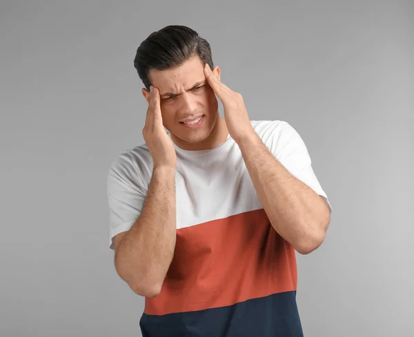 Junger Mann mit Kopfschmerzen auf grauem Hintergrund — Stockfoto