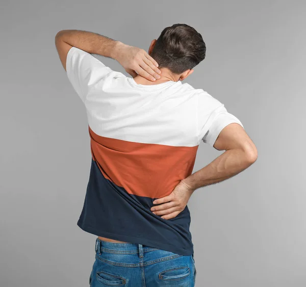 Young man suffering from back pain on grey background — Stock Photo, Image