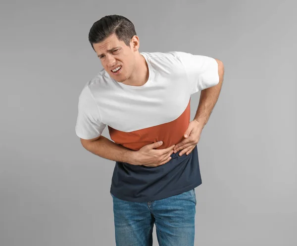 Young man suffering from abdominal pain on grey background — Stock Photo, Image