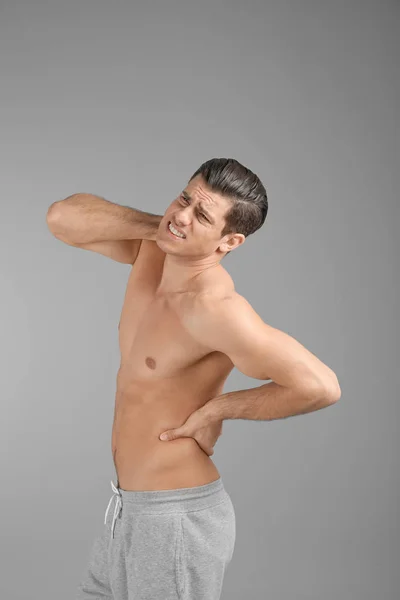 Junger Mann mit Rückenschmerzen vor grauem Hintergrund — Stockfoto