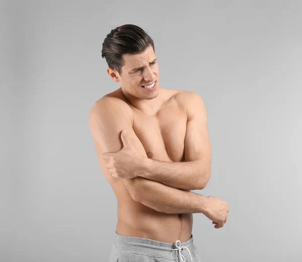 Junger Mann leidet unter Schmerzen im Arm vor grauem Hintergrund — Stockfoto