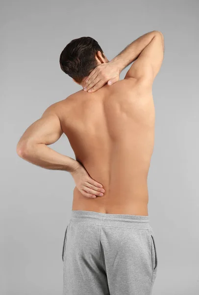 Young man suffering from back pain on grey background — Stock Photo, Image