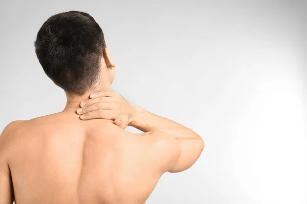 Young man suffering from neck pain on light background — Stock Photo, Image