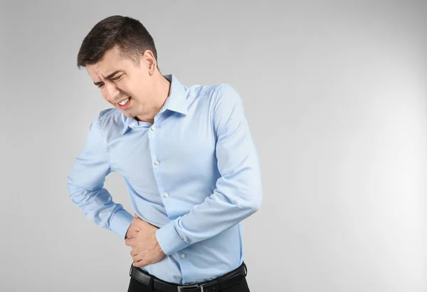 Young man suffering from flank pain on light background — Stock Photo, Image
