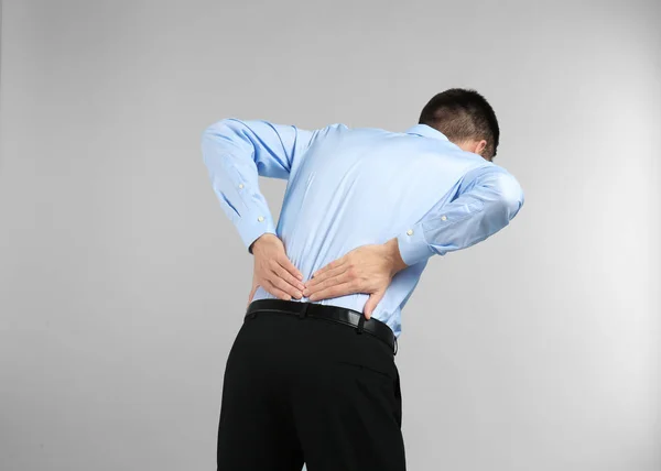 Junger Mann mit Rückenschmerzen vor hellem Hintergrund — Stockfoto