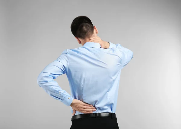 Young man suffering from back pain on light background — Stock Photo, Image