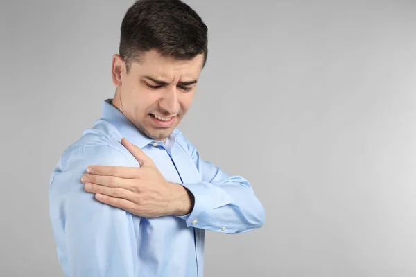 Young man suffering from pain in shoulder on light background — Stock Photo, Image