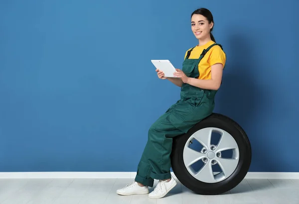 Mecânico feminino em uniforme com pneu de carro e tablet no fundo da parede de cor — Fotografia de Stock