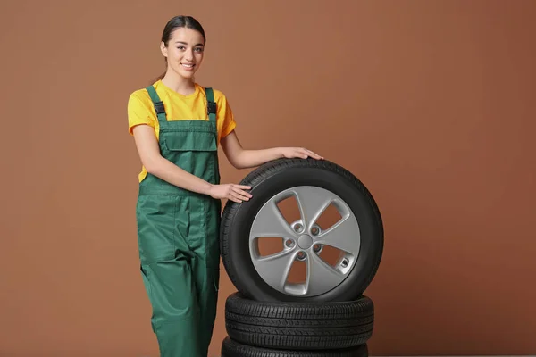 Mecânico feminino em uniforme com pneus de carro no fundo de cor — Fotografia de Stock