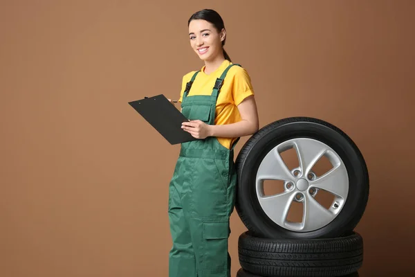 Feminino mecânico em uniforme com pneus de carro e área de transferência em fundo de cor — Fotografia de Stock