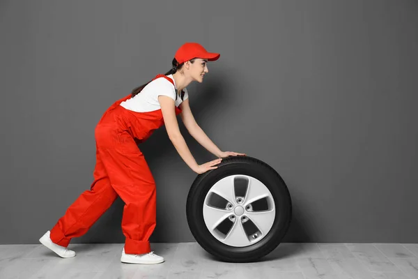 Feminino mecânico em uniforme com pneu de carro no fundo da parede cinza — Fotografia de Stock