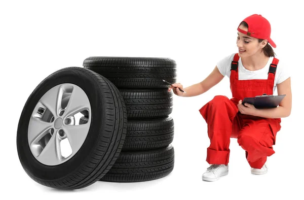 Mecánica femenina en uniforme con neumáticos de coche y portapapeles sobre fondo blanco — Foto de Stock