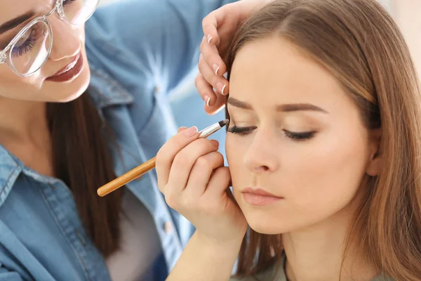 Artista de visagem profissional aplicando maquiagem no rosto da mulher no salão — Fotografia de Stock