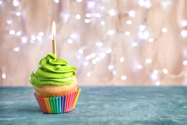 Birthday cupcake with burning candle on table against blurred lights — Stock Photo, Image