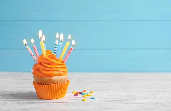 Delicioso cupcake de cumpleaños con velas encendidas en la mesa contra el fondo de color —  Fotos de Stock