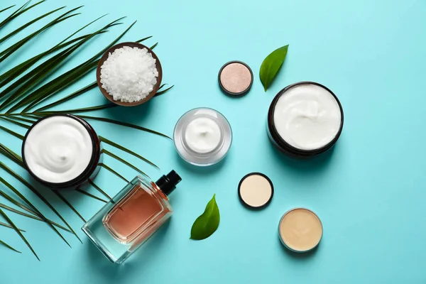 Diferentes productos cosméticos para el cuidado de la piel con hojas verdes sobre fondo de color, vista superior — Foto de Stock