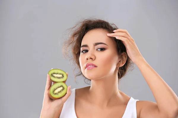 Mooie jonge vrouw met acne probleem bedrijf kiwi op grijze achtergrond. Allergie huid — Stockfoto