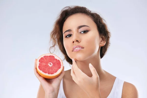 Mooie jonge vrouw met acne probleem bedrijf grapefruit op lichte achtergrond. Allergie huid — Stockfoto