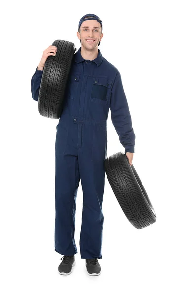 Joven mecánico en uniforme sosteniendo neumáticos de coche sobre fondo blanco — Foto de Stock