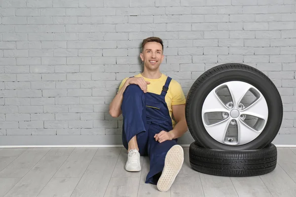 Mecânico masculino com pneus de carro no fundo da parede de tijolo — Fotografia de Stock