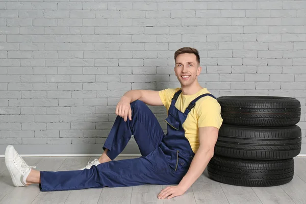 Mecánico masculino con neumáticos de coche sobre fondo de pared de ladrillo —  Fotos de Stock