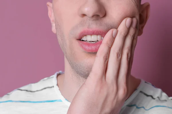 Jeune homme avec des dents sensibles sur fond de couleur, gros plan — Photo
