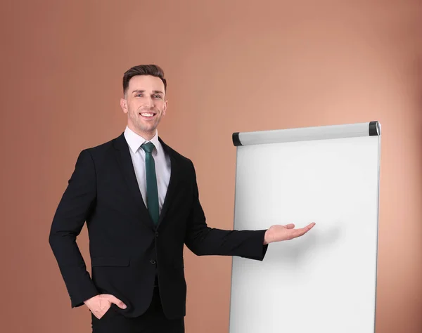 Junger Business-Trainer in der Nähe von Flipchart auf farbigem Hintergrund — Stockfoto