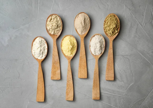 Spoons with different types of flour on gray background — Stock Photo, Image