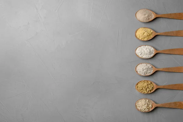 Cucharas con diferentes tipos de harina sobre fondo gris — Foto de Stock