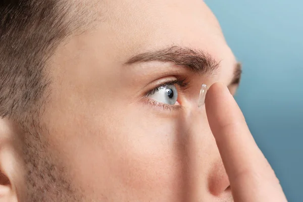 Ung man sätta kontaktlins i ögat på färgbakgrund — Stockfoto