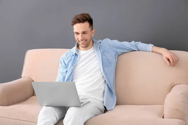 Schöner junger Mann mit Laptop auf Sofa sitzend, drinnen — Stockfoto