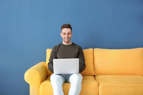 Jovem bonito com laptop sentado no sofá, dentro de casa — Fotografia de Stock