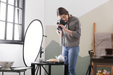 Profesyonel kameralı genç bir kadın stüdyoda yemek fotoğrafı çekiyor.