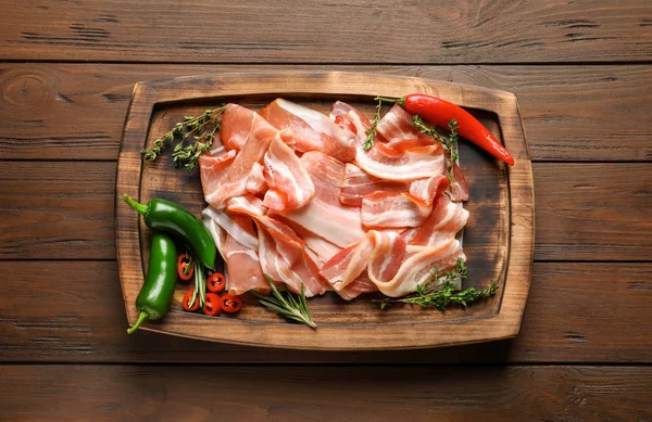 Board with raw bacon rashers on wooden background