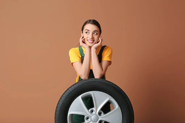 Mecânico feminino em uniforme com pneu de carro no fundo de cor — Fotografia de Stock