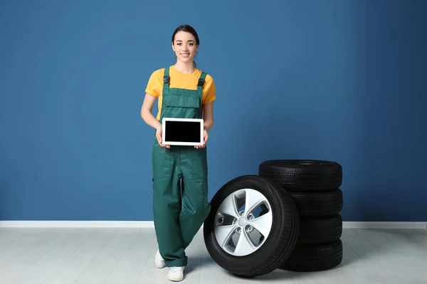 Mecânico feminino em uniforme com pneus de carro e tablet no fundo da parede de cor — Fotografia de Stock