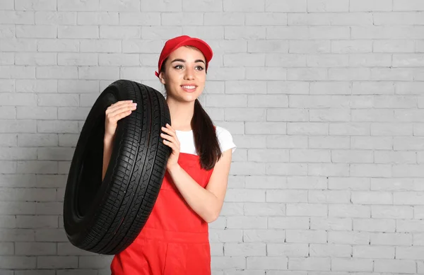 Vrouwelijke monteur in uniform met auto band tegen een bakstenen muur achtergrond — Stockfoto