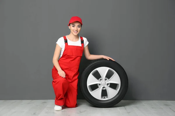 Feminino mecânico em uniforme com pneu de carro no fundo da parede cinza — Fotografia de Stock