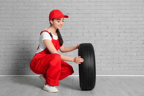 Vrouwelijke monteur in uniform met auto band tegen een bakstenen muur achtergrond — Stockfoto