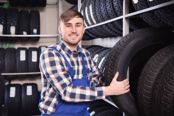 Jovem mecânico masculino com pneus de carro no centro de serviços de automóveis — Fotografia de Stock