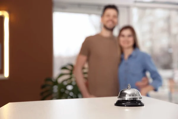 Hotel service bell on reception desk and blurred young couple on background