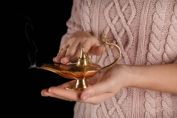 Young woman rubbing Aladdin magic lamp on black background, closeup — Stock Photo, Image
