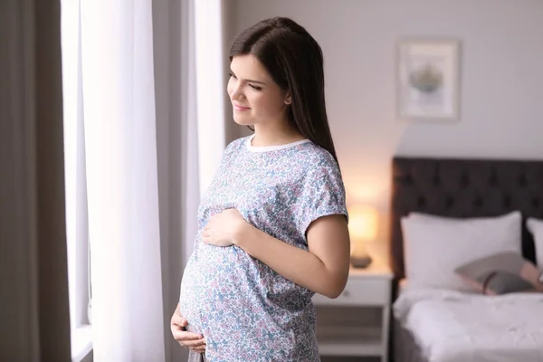 Jonge zwangere vrouw bij het raam thuis — Stockfoto