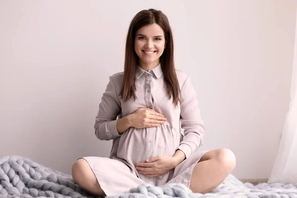 Молодая беременная женщина сидит на теплом одеяле в помещении — стоковое фото