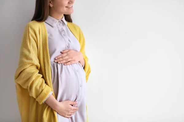 Młoda kobieta w ciąży w ubranie na jasnym tle — Zdjęcie stockowe