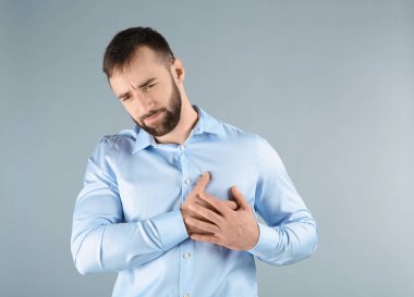Genç adam ışık arka plan üzerinde göğüs ağrısı muzdarip