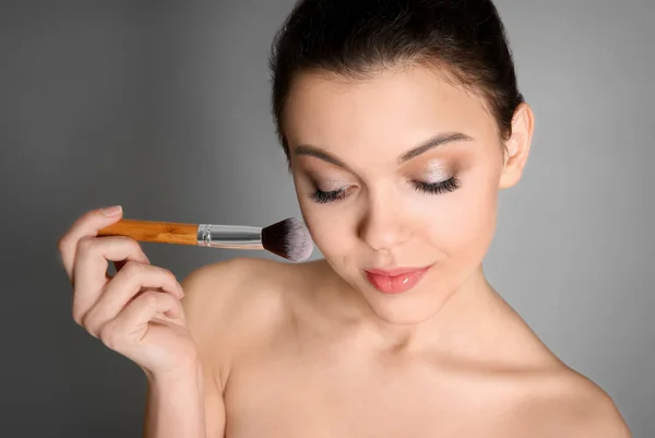 Młoda kobieta stosowania makijażu na szarym tle. Profesjonalne kosmetyki — Zdjęcie stockowe